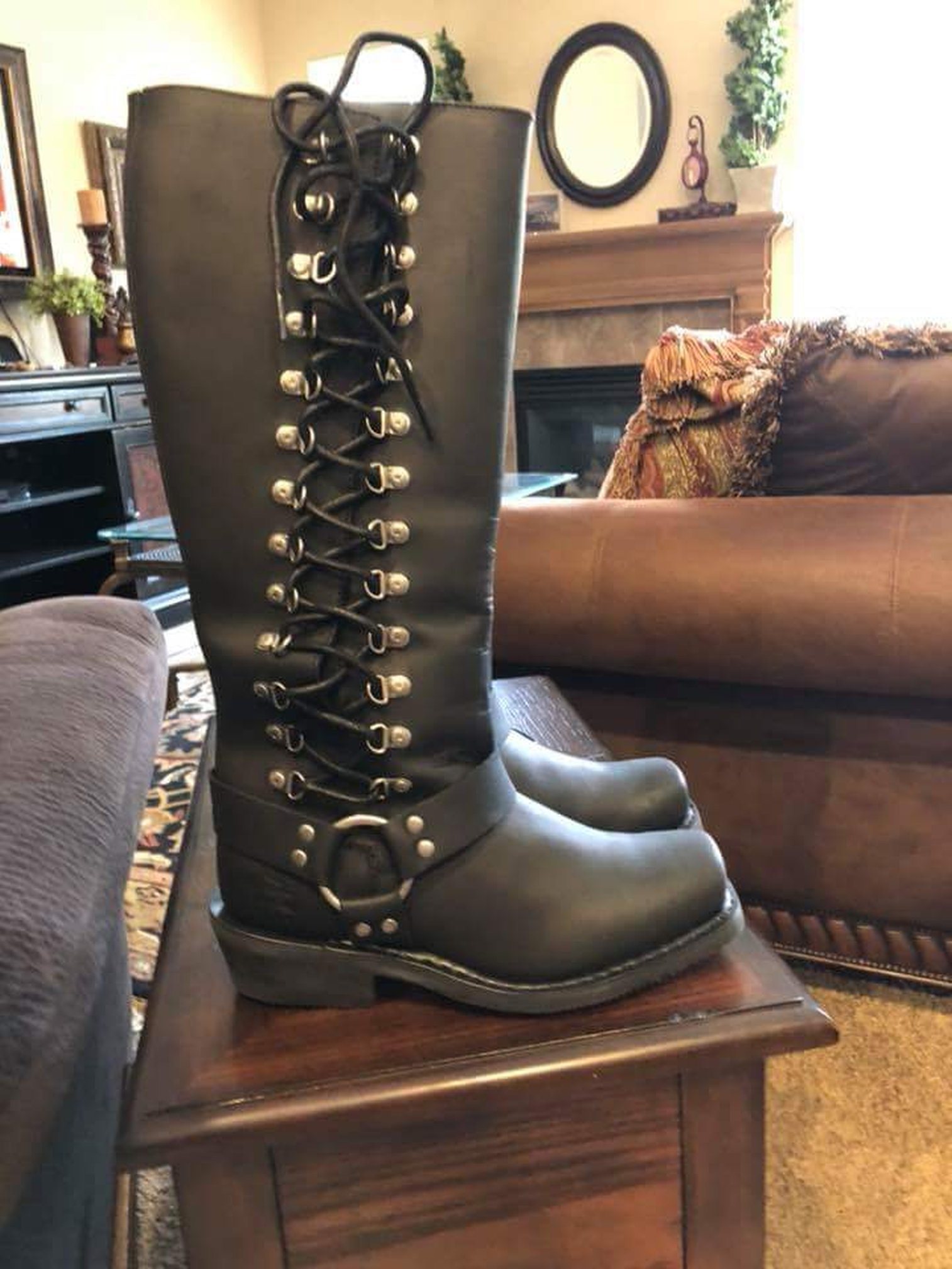 Especially long Harley-Davidson brand boots with a thick sole. Laces run up the outside of the leg from ankle to calf, through heavy duty D rings. A leather strap at the ankle locates to a heavy silver ring on the outside ankle..
