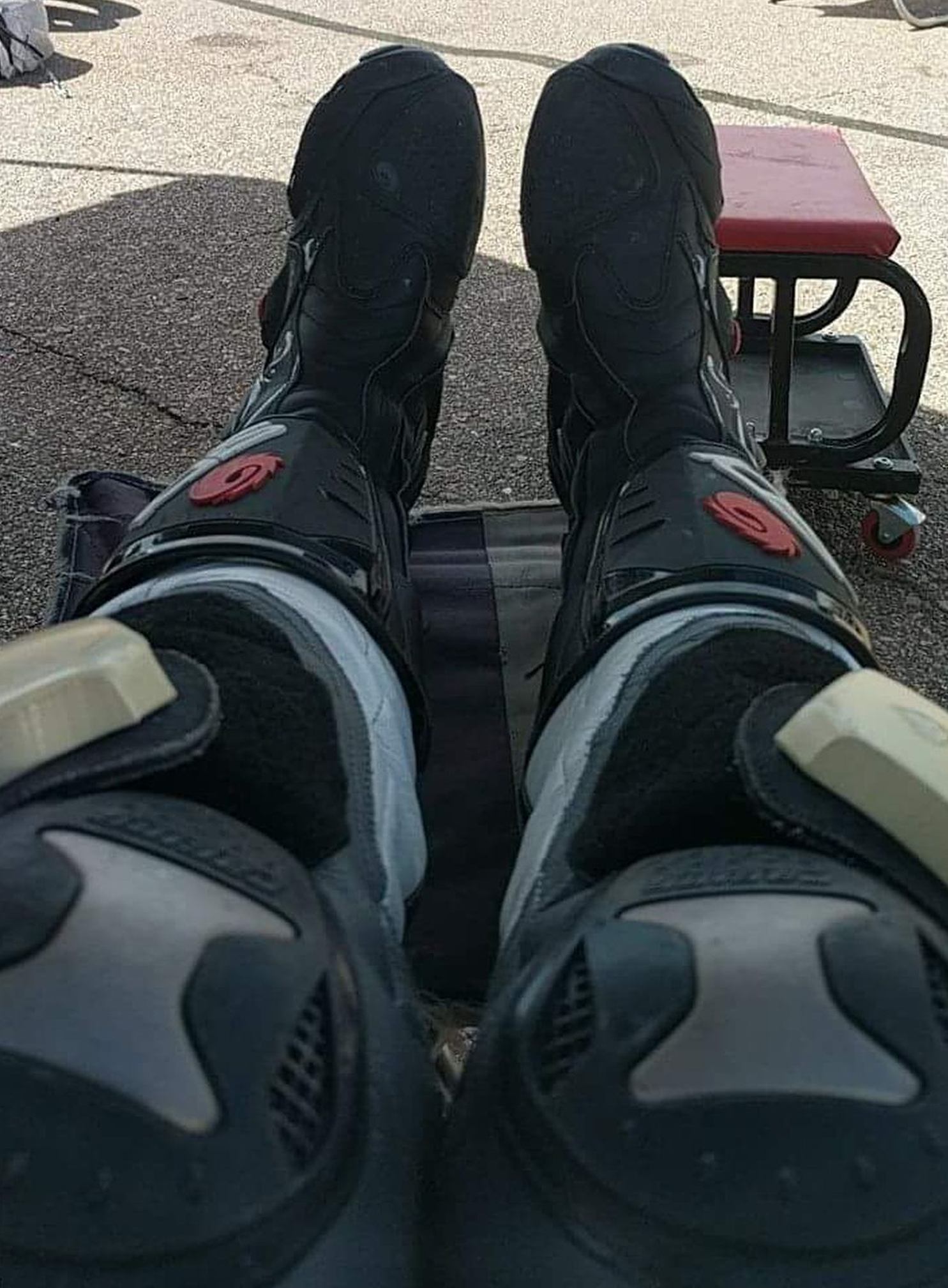 A mans legs extending from the foreground, dressed in armored knee pads and shin guards, with heavy duty sport/MX boots on his feet. Thick "drag pads" adorn the knees.