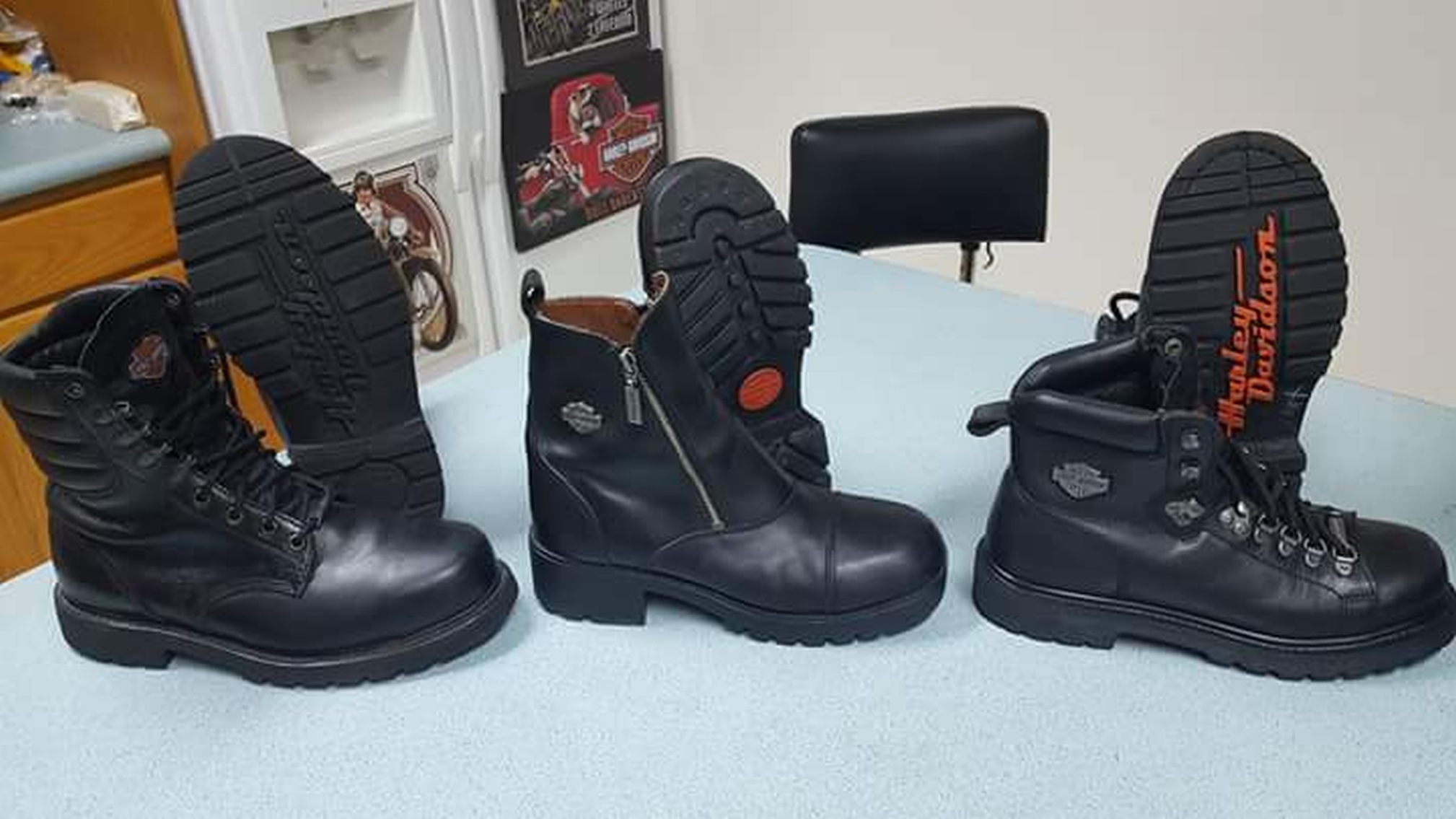 Three pairs of black leather boots pictures on a blue field. Of each pair the right boot is sitting normally while the left is propped against it's twin to show the tread. Two pairs on the ends are traditional lace-up engineer boots, the middle zip-up street boots. Emblazoned on the underside of one pair in red is the brand name.
