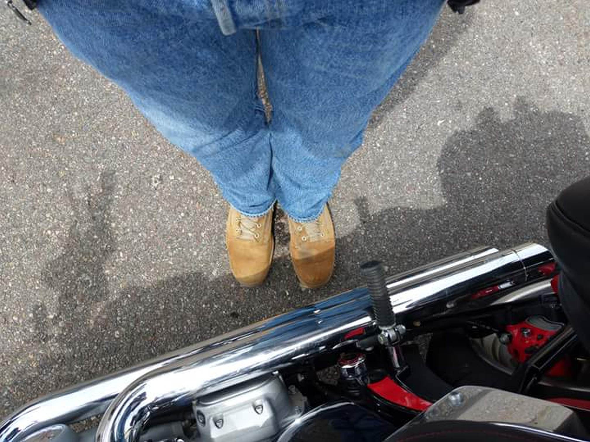 Top-down view of a man wearing rugged tan hiking boots with thick laces, next to a motorcycle.