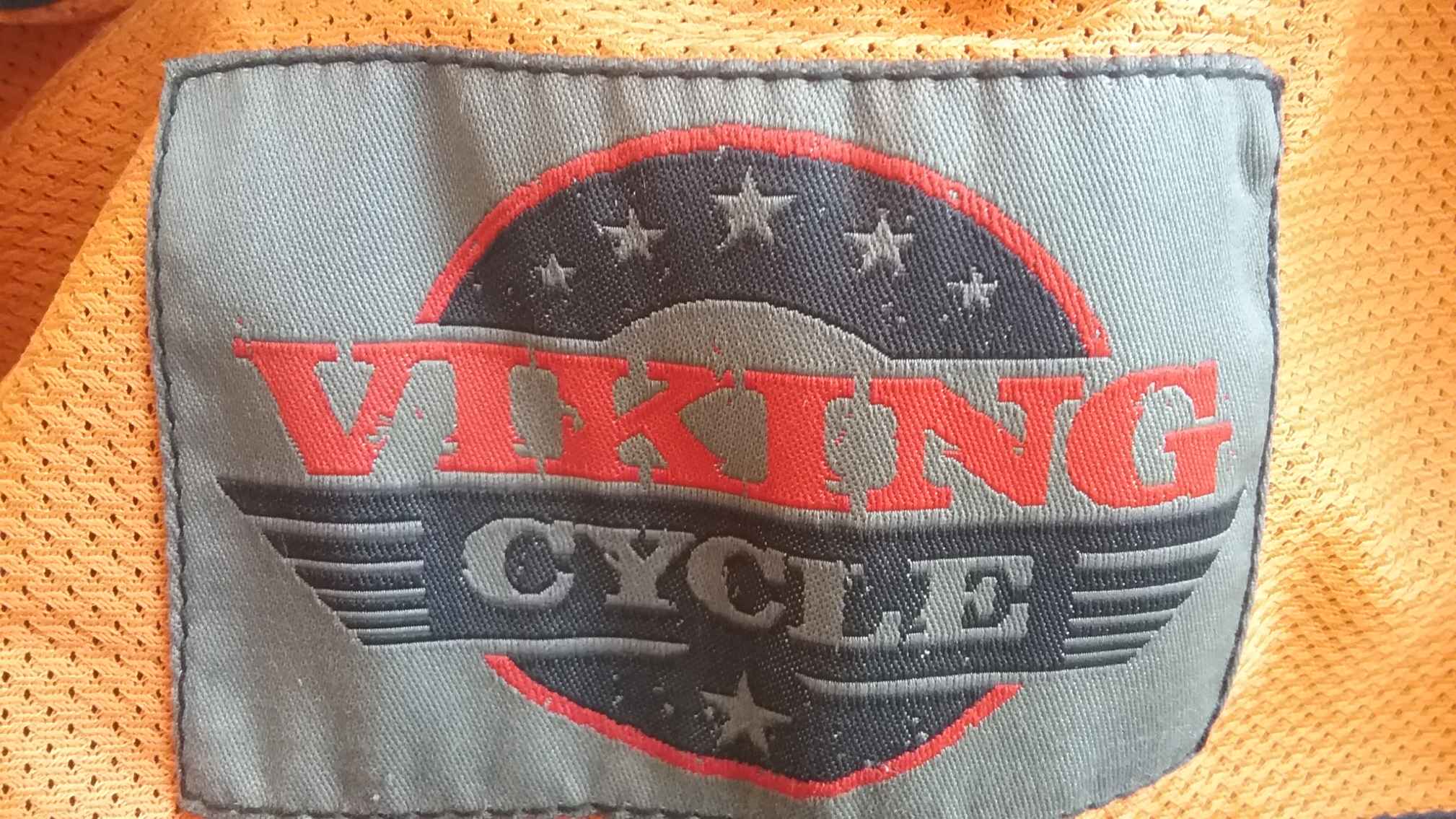 An extreme close-up of the inside lining of a leather vest. A gray, black and red label displays the manufacturers logo "Viking Cycle", on a perforated orange background.