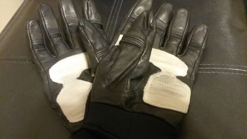 Indian Women's Review, A pair of sturdy looking black leather gloves lie palm side up, the palms are reinforced with a layer of white leather that are marked with minimal black scuff marks.