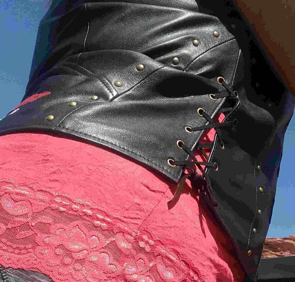 Indian Women's Review, A close up view of the side of a woman's torso, she is wearing a black leather motorcycle vest with laced up sides, the vest seams are embellished with antiqued brass rivets.