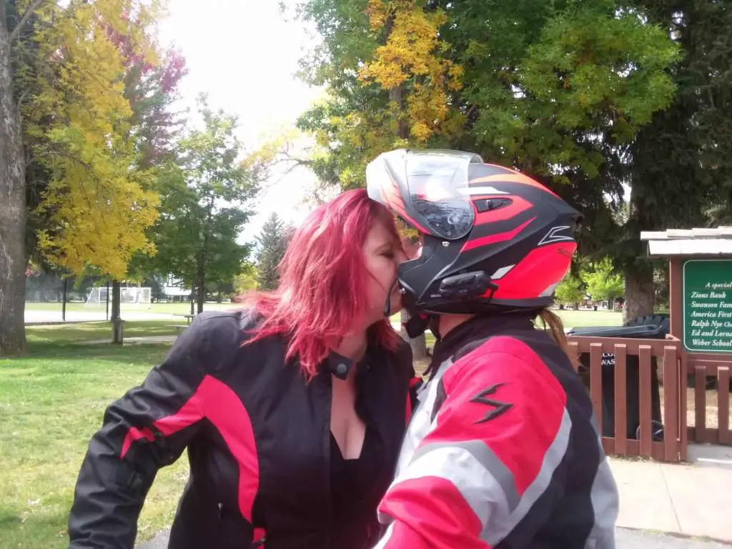 With the helmet face in the upright position, the rider kisses his lovely wife.