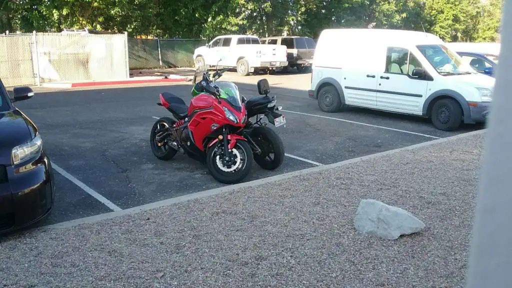 A Kawasaki Ninja 650R and Kawasaki Versys 650 are pictured, parked in a motel lot. They are arranged head to toe with each other, extremely close together.