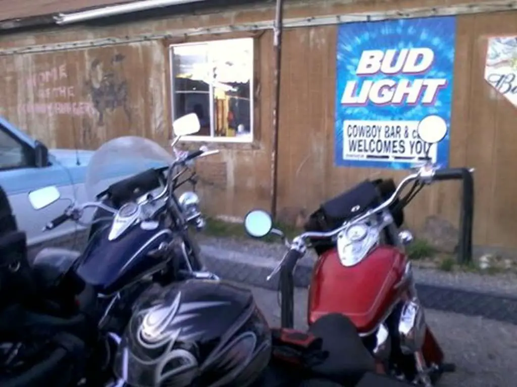Red Honda Shadow and blue Kawasaki Vulcan parked outside a weathered clapboard tavern. The image is grainy and out of focus.