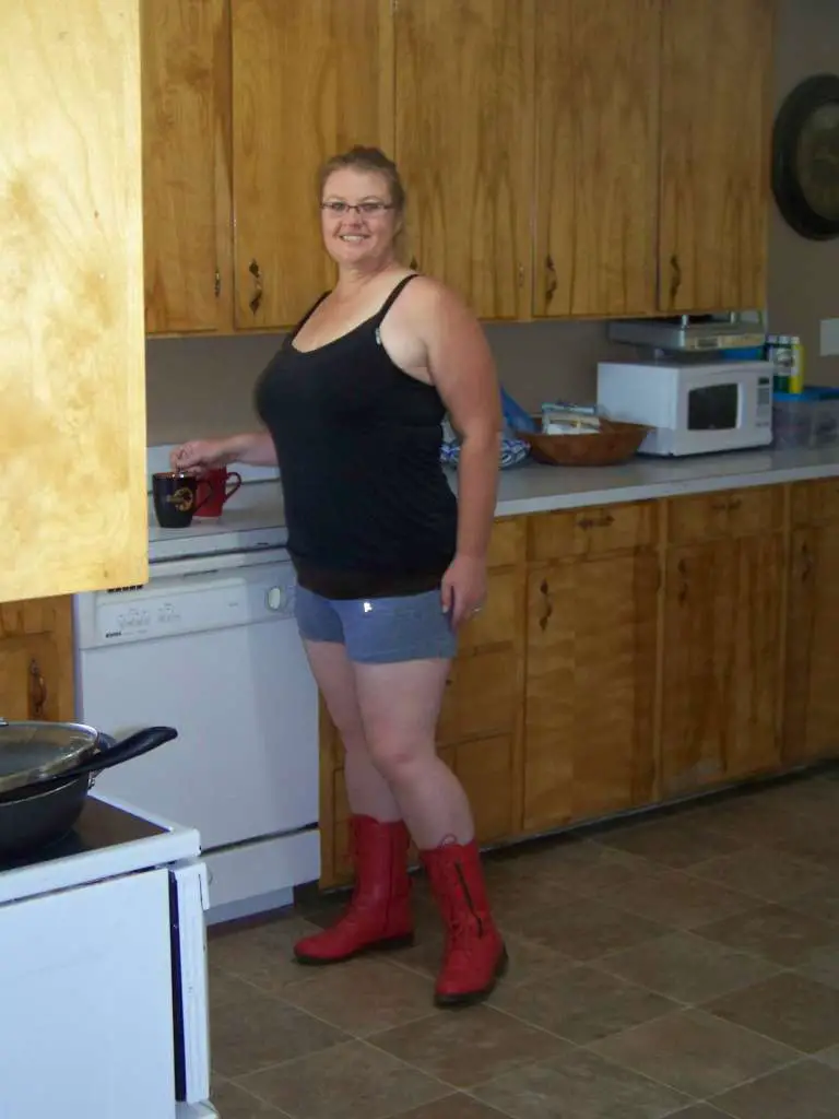 Staff writer Carrie Leaverton pictured in a rustic kitchen setting. She is wearing a casual black tank top, gray pajama shorts and bright red motorcycle boots.