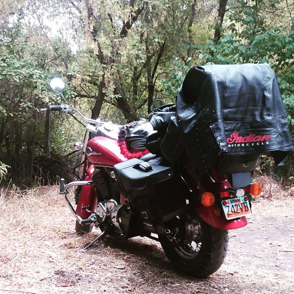 A shiny red and chrome Honda Shadow Motorcycle is parked in a clearing in the woods with black leather luggage packed onto the pillion and luggage rack.
