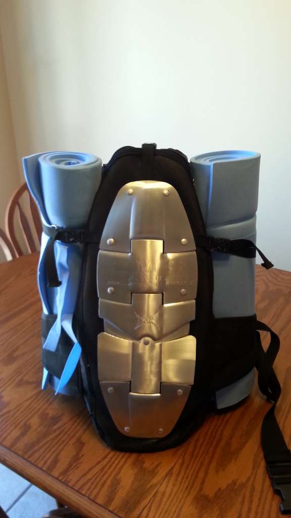 A backpack sits atop a table with 2 bedrolls strapped vertically on either side.