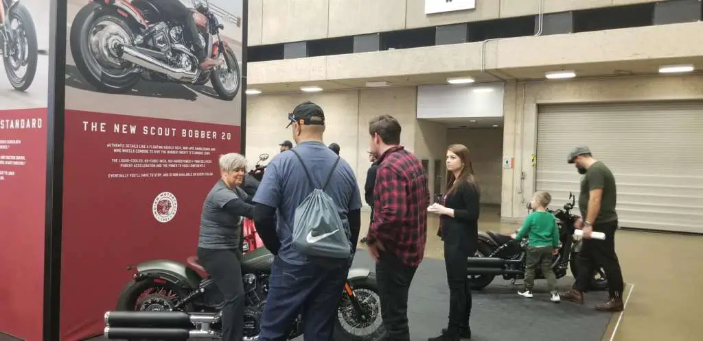 Several people mill around the Indian Scout Bobber display.