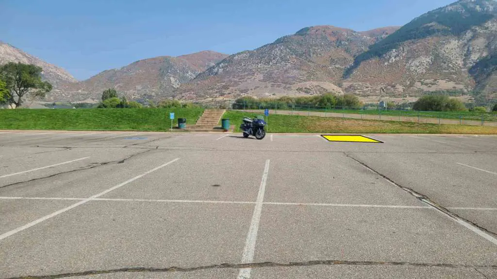 A parking lot is pictured with dramatic mountains in the background. Centered is a Honda CTX 1300. The second parking stall to the right is highlighted in yellow.
