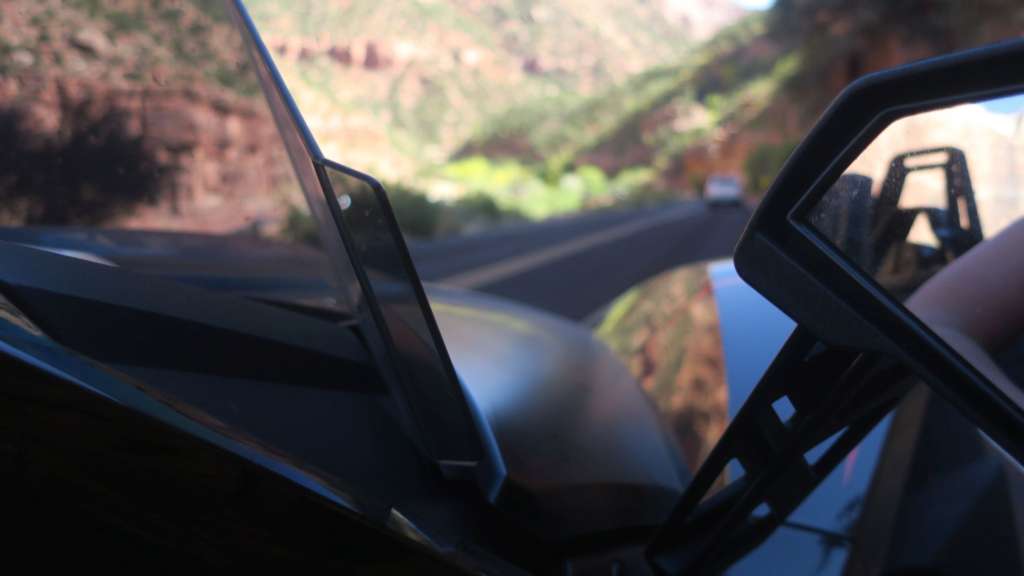 A tight angle shot from between the windshield and rearview mirror of the Slinghsot R. In the background, a blurred canyon road with rugged scenery.
