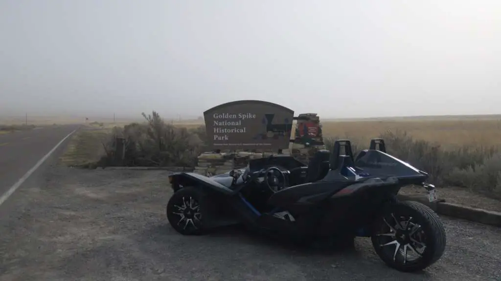 Pictured is the 2021 Slingshot S in a quaint gravel parking lot. A marquee behind says "Golden Spike National Historical Park.