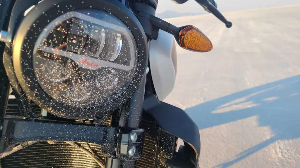 Close-up of the headlight of the 2022 Indian FTR-S. The headlight is covered in a spray of fine salt from the flats.